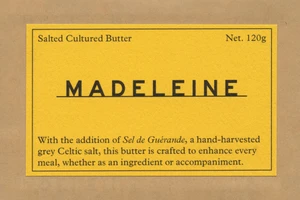 Yellow product label with black typography for Madeleine butter centered on textured brown paper.