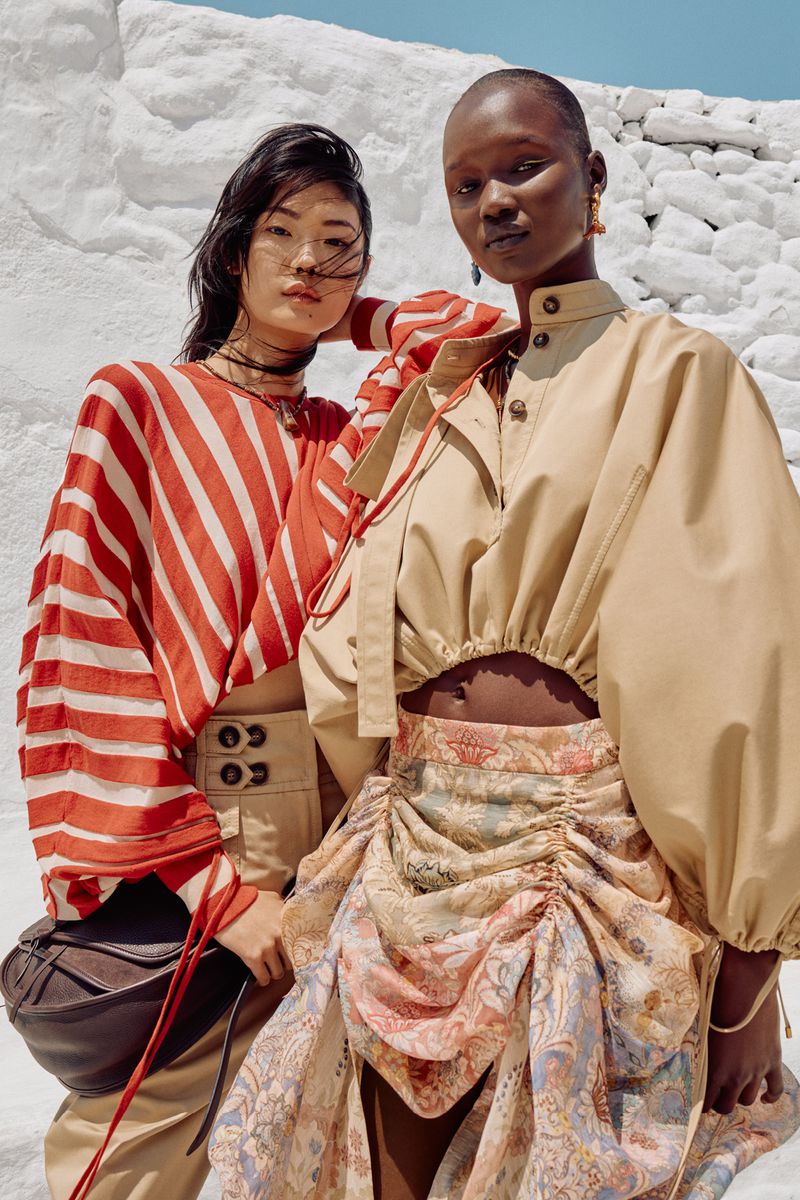 Two models pose in outdoor fashion shot with bold stripes and a draped skirt, against a white background, showcasing modern, high-end apparel.