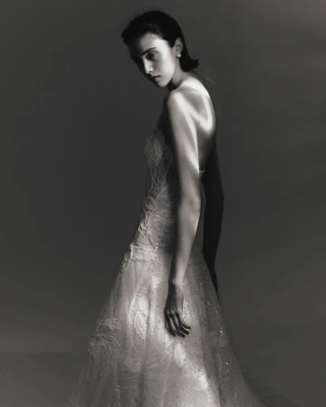 Model Sandra Formanek wearing a strapless embellished lace gown in dramatic studio lighting against a dark grey backdrop.