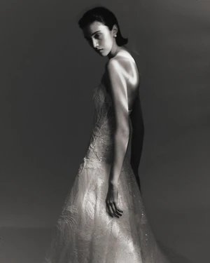 Model Sandra Formanek wearing a strapless embellished lace gown in dramatic studio lighting against a dark grey backdrop.