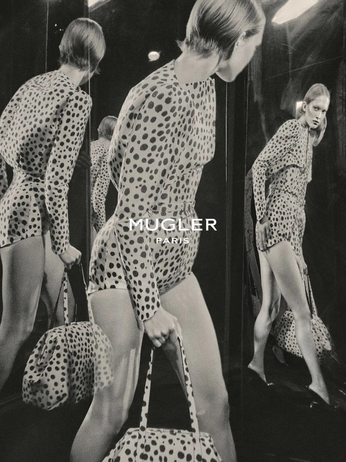 Model in spotted bodysuit holding matching bag reflected in multiple mirrors for Mugler