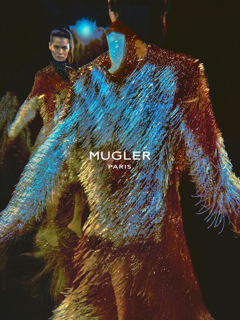 Model in iridescent fringed garment with the Mugler Paris logo centered against a dark background
