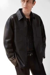 Man wearing a black leather shirt jacket over a dark patterned shirt against a plain white background