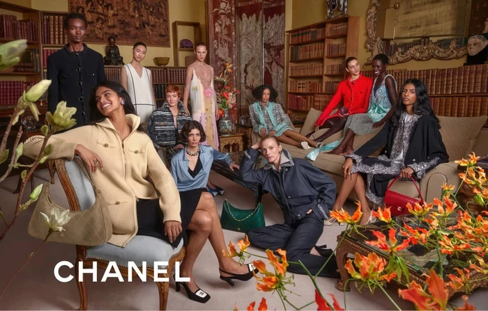 Group of models in Chanel apparel gathered in a warmly lit historic room filled with bookshelves.