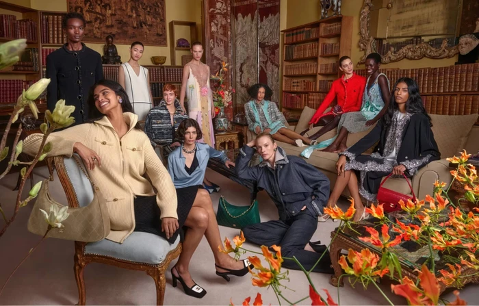 Group of diverse fashion models posed inside a wood-paneled room with bookshelves and floral arrangements for Chanel