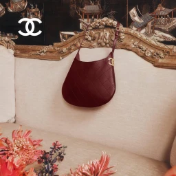 Burgundy quilted leather handbag hung against an ornate vintage sofa with floral arrangements and a black lacquer screen backdrop