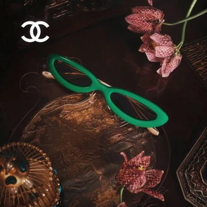 Green sunglasses resting on an ornate carved tray with pink checkered flowers and the Chanel logo in the corner
