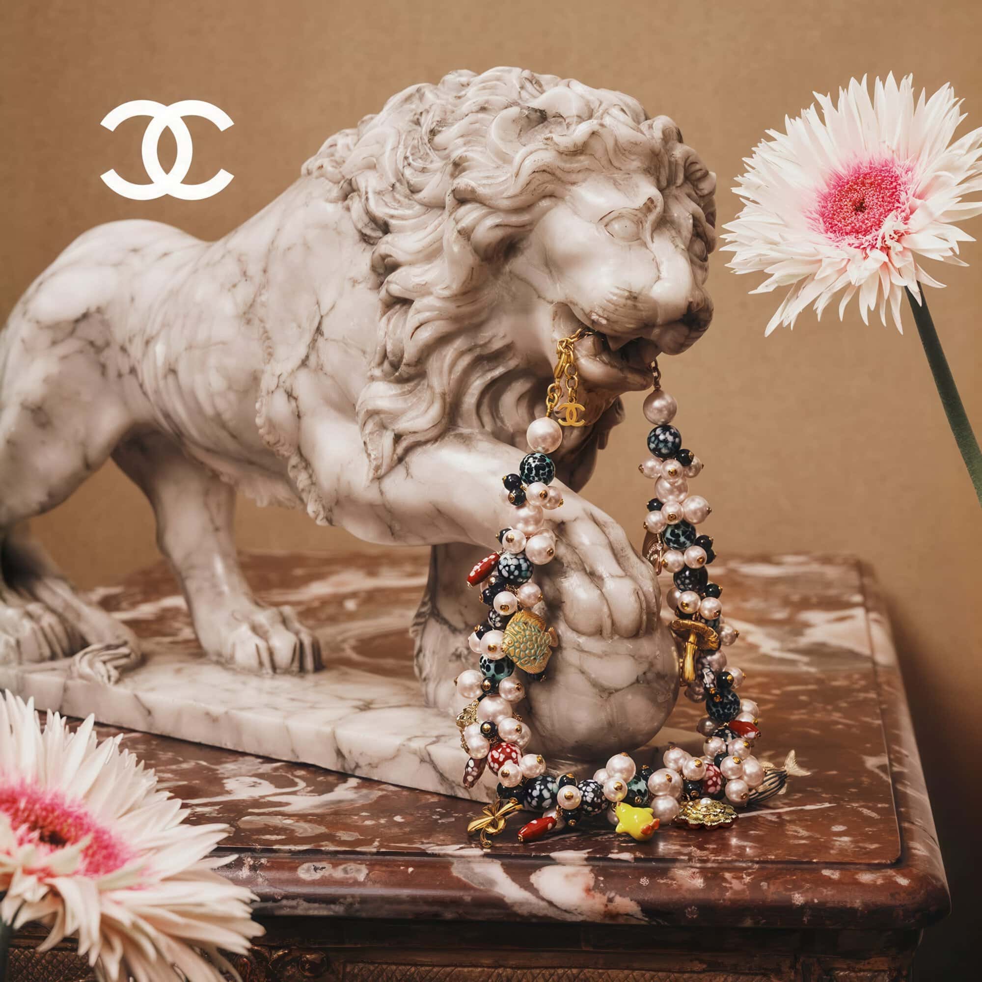 Marble lion statue holding a pearl and bead necklace in its mouth on a marble table with white and pink gerbera flowers