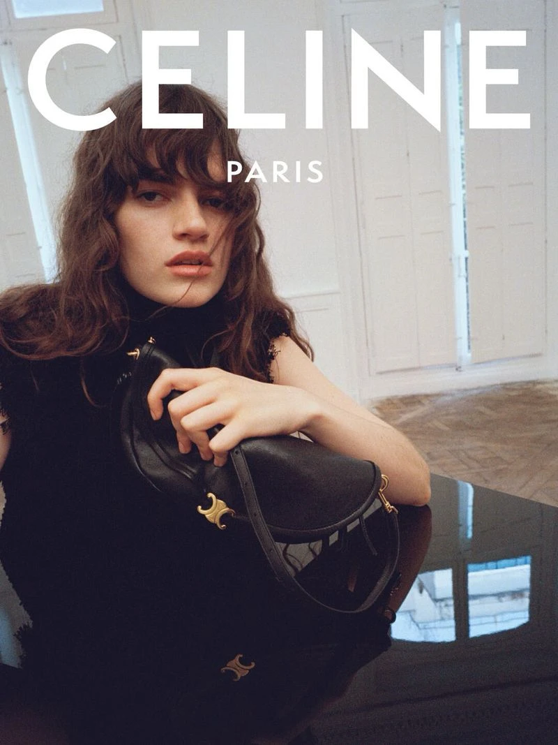 Model holding a black leather handbag with gold hardware against a light interior background for Celine Spring 2027.