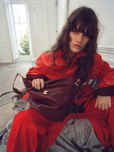 Model in red leather jacket holding a burgundy leather handbag inside a bright room