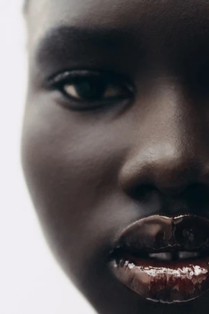Extreme close-up beauty portrait of model Nyakong Chan featuring glossy dark lips against a white background.