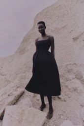 Model wearing a black midi dress standing against a rocky stone cliff background
