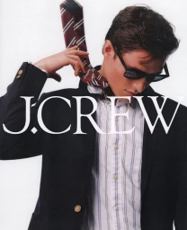 Man adjusting striped necktie wearing a dark blazer and sunglasses against a white background for J. Crew by Dudi Hasson