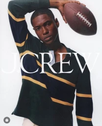 Man holding a brown football overhead wearing a green striped rugby shirt against a plain white background for J. Crew