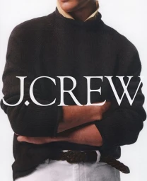 Model wearing a dark knit sweater and white pants with the word J.Crew overlaid horizontally across the chest.