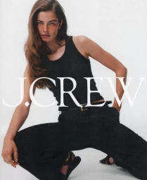 Model wearing a black tank top and dark pants squatting against a plain white background with bold J.Crew text overlay.