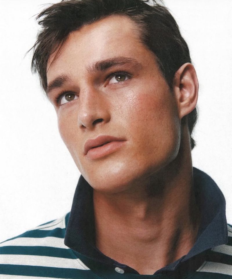 Close-up portrait of a male model wearing a striped polo shirt against a plain white background, photographed by Dudi Hasson for J. Crew.