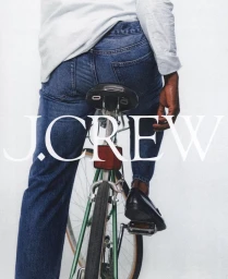Person straddling a green bicycle wearing blue jeans, a white long-sleeve shirt, and black loafers against a white backdrop.