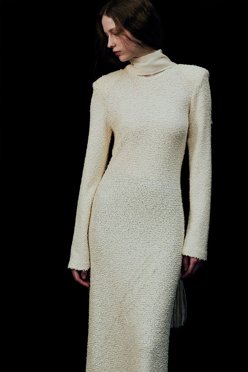 Model wearing a long-sleeved textured cream dress with a high collar against a dark background