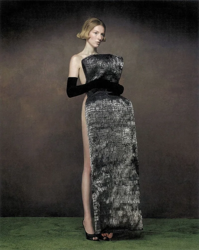 Hunter Schafer wearing a sculptural textured black dress and long gloves standing against a textured backdrop