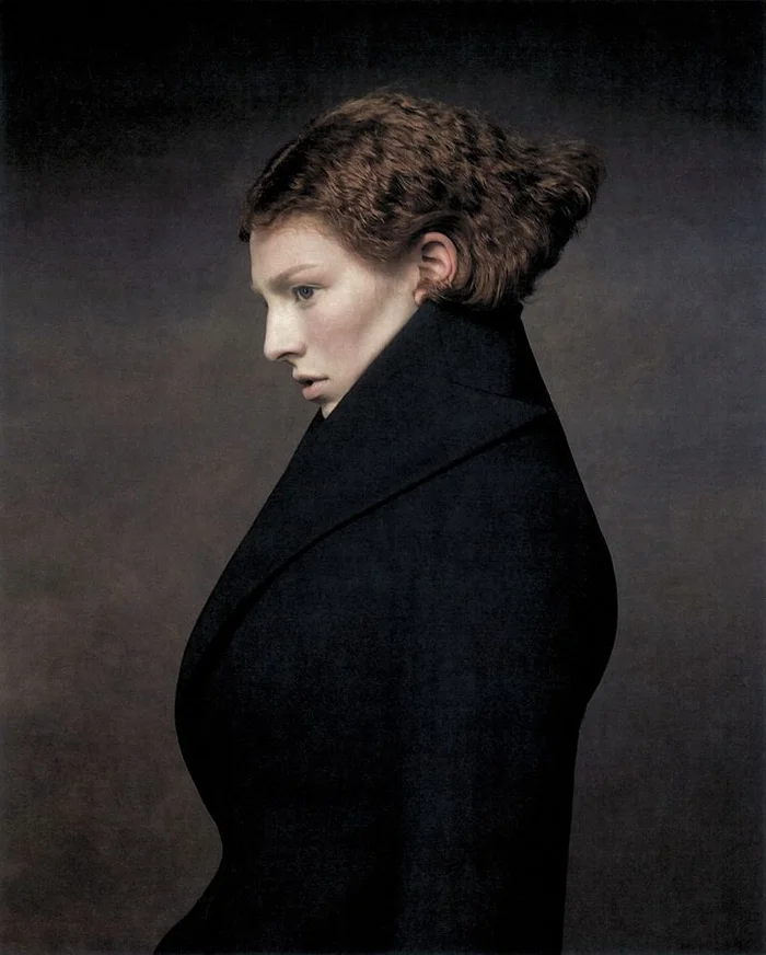 Hunter Schafer in profile wearing a high-collared black coat against a dark, textured background for Elle U.S.