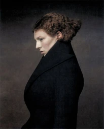 Hunter Schafer in profile wearing a high-collared black coat against a dark, textured background for Elle U.S.