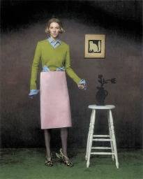 Hunter Schafer wearing a green sweater and pink skirt standing next to a small white stool in an Elle U.S. editorial shoot