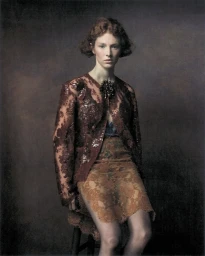 Hunter Schafer wearing a textured burgundy lace jacket and skirt against a dark muted background for Elle U.S.