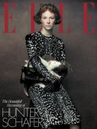 Hunter Schafer seated wearing a black and white patterned dress holding a toy rat and a black handbag
