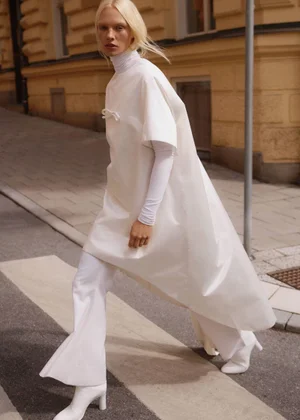 Model Vilma Sjoberg walking outdoors in a white poncho and trousers for Elle Sweden