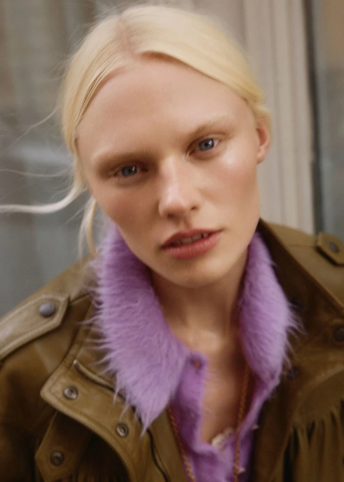 Close-up portrait of blonde model Vilma Sjöberg wearing an olive jacket with a fluffy purple collar for Elle Sweden