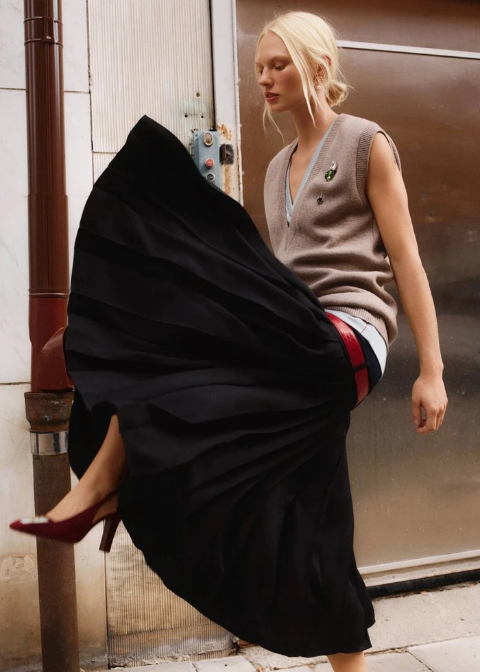 Model Vilma Sjoberg wearing a brown sweater vest and black pleated skirt outdoors for Elle Sweden