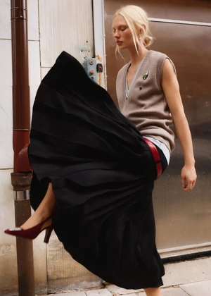 Model Vilma Sjoberg wearing a brown sweater vest and black pleated skirt outdoors for Elle Sweden