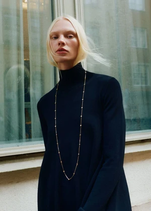 Model Vilma Sjöberg wearing a black turtleneck and long necklace against a building exterior with windows.