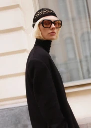 Model Vilma wearing a black turtleneck and net cap with sunglasses against a building exterior.