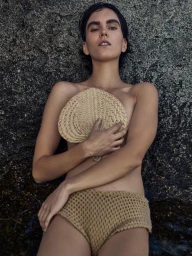Model Polina Park lying against a dark textured rock holding a woven straw fan for Elle Bulgaria photography