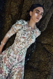 Model in intricate floral embroidered sheer gown reclining against dark rock surface