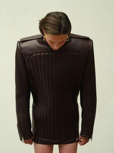 Model wearing a structured dark brown leather jacket with prominent shoulder pads against a seamless backdrop