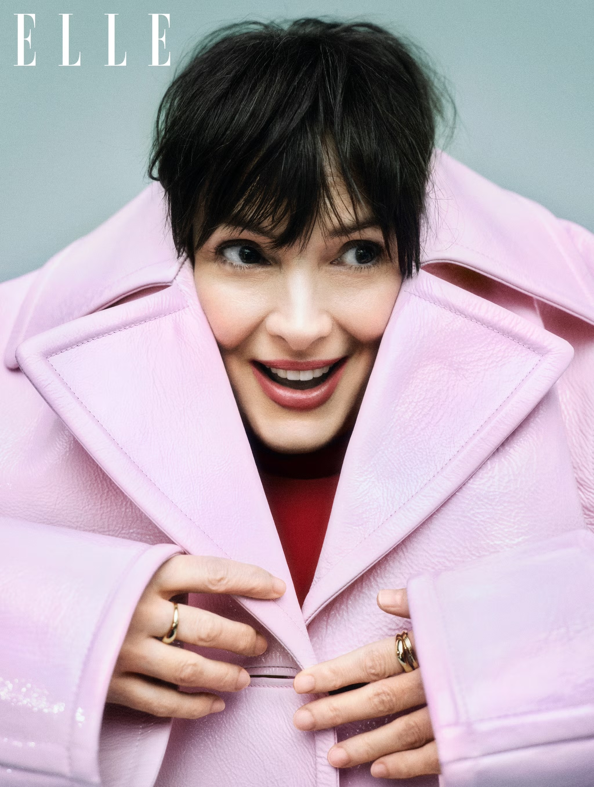 Winona Ryder wearing an oversized pink coat and red top against a grey background for Elle UK.