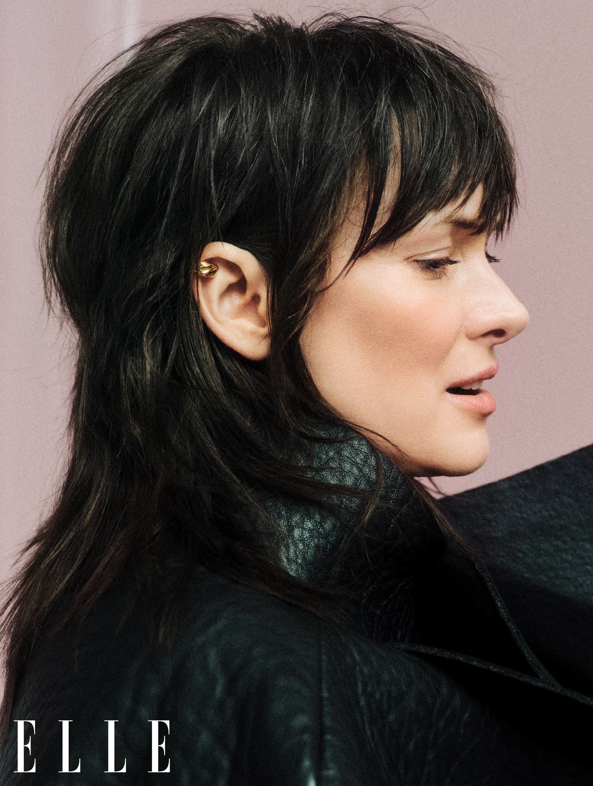 Close-up profile of a woman with a dark mullet haircut wearing a black leather jacket against a light pink background, with 'ELLE' logo.