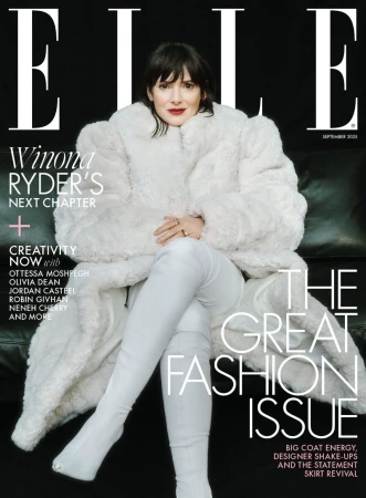 Winona Ryder seated on a dark leather couch wearing an oversized white fur coat and matching white boots for Elle UK.