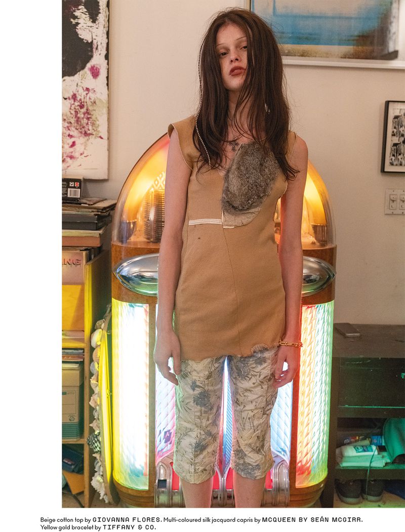 Model Scarlett White standing in front of an illuminated vintage jukebox wearing a beige top and patterned capris