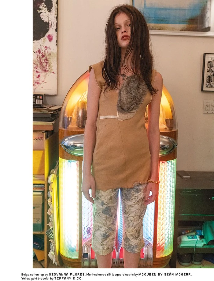 Model Scarlett White standing in front of an illuminated vintage jukebox wearing a beige top and patterned capris