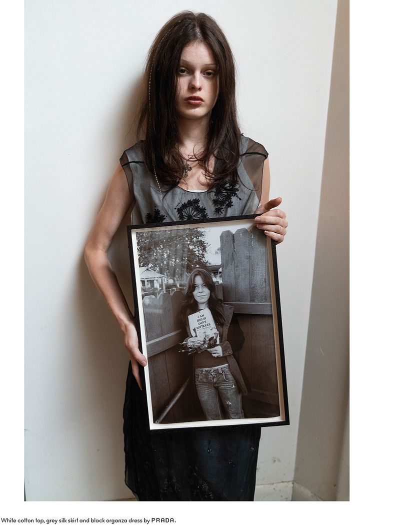 Model Scarlett White holding a framed black and white photograph against a plain wall for Beyond Noise editorial.