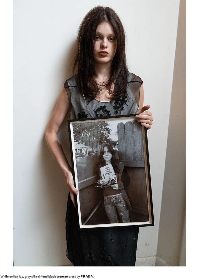 Model Scarlett White holding a framed black and white photograph against a plain wall for Beyond Noise editorial.