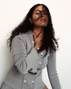 Model Ylang Messenguiral wearing a grey knit cardigan with white buttons against a plain white background for M Le magazine du Monde.