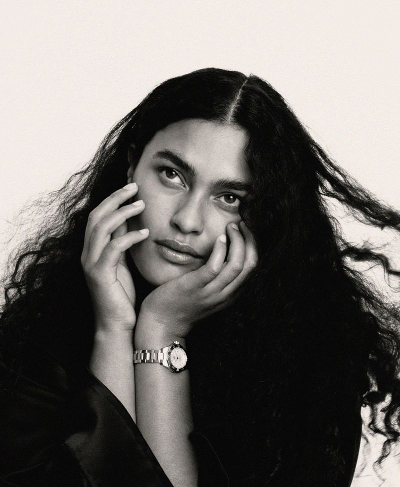 Model Ylang Messenguiral with long dark curly hair wearing a metal wristwatch with hands framing her face