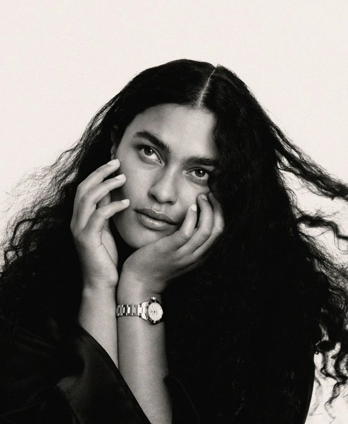 Model Ylang Messenguiral with long dark curly hair wearing a metal wristwatch with hands framing her face