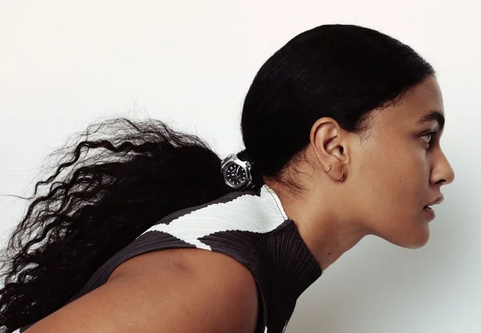 Profile portrait of a woman with dark curly hair tied back wearing a patterned top against a plain white background