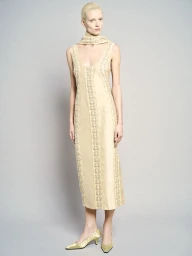 Model standing against a neutral grey backdrop wearing a sleeveless patterned midi dress and matching scarf with heeled shoes.